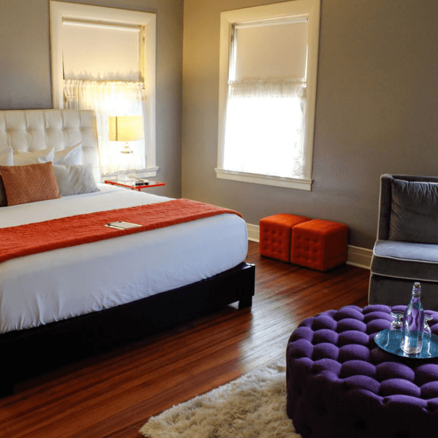 A cozy bedroom featuring a white upholstered bed, orange accents, and a purple ottoman.