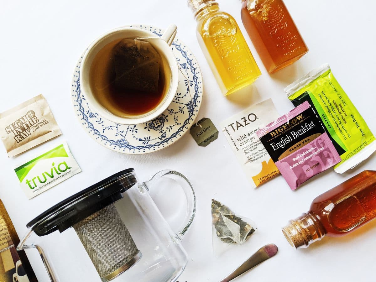 A cup of tea surrounded by various sweeteners, tea bags, and honey bottles on a white surface.